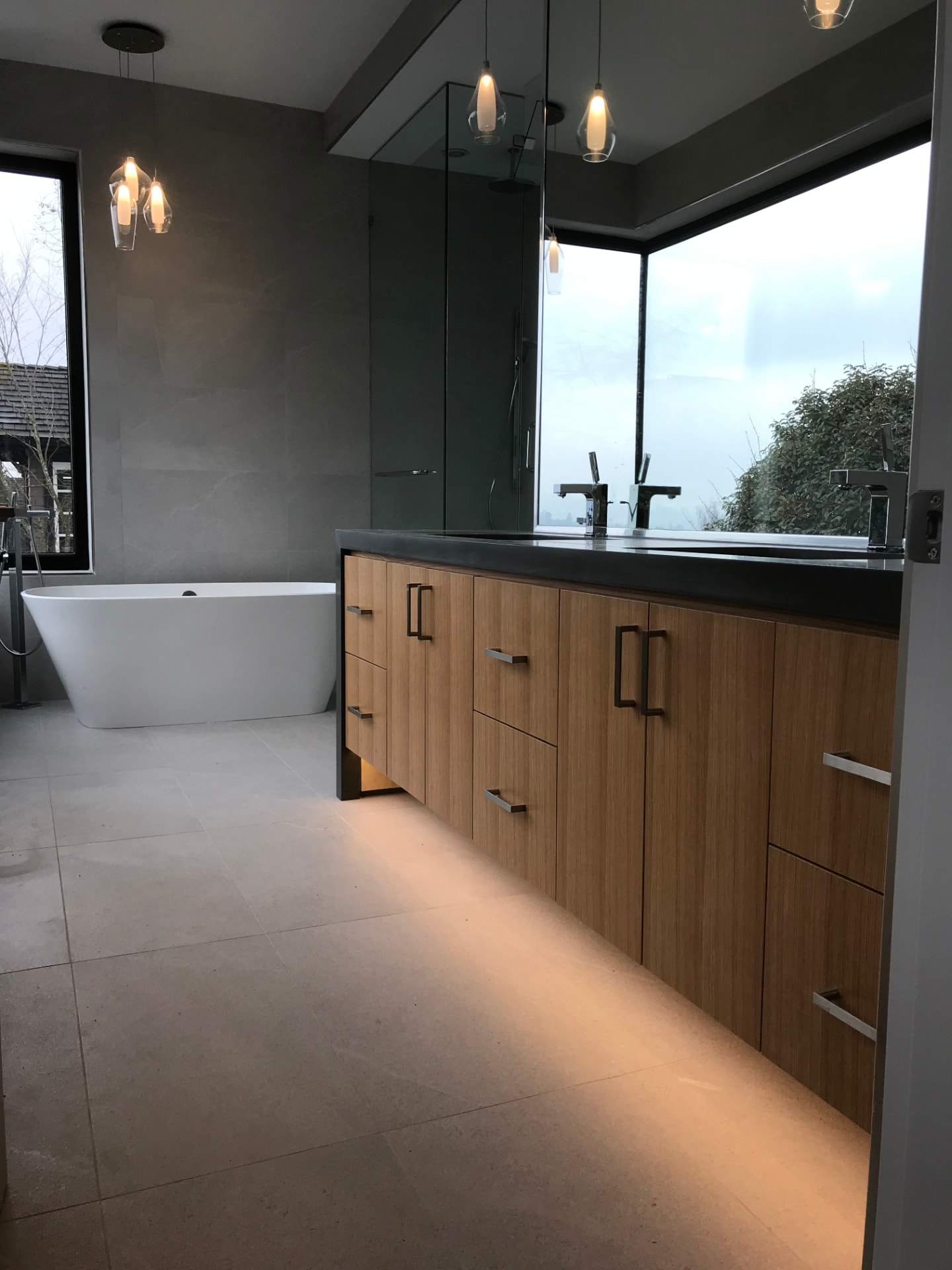 Walnut bathroom vanities with dark charcoal counters, pendant lights, and large mirrors