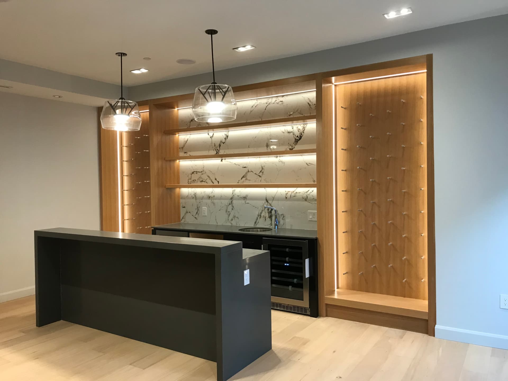 Custom walnut wine display and home bar with a charcoal island and marble backsplash