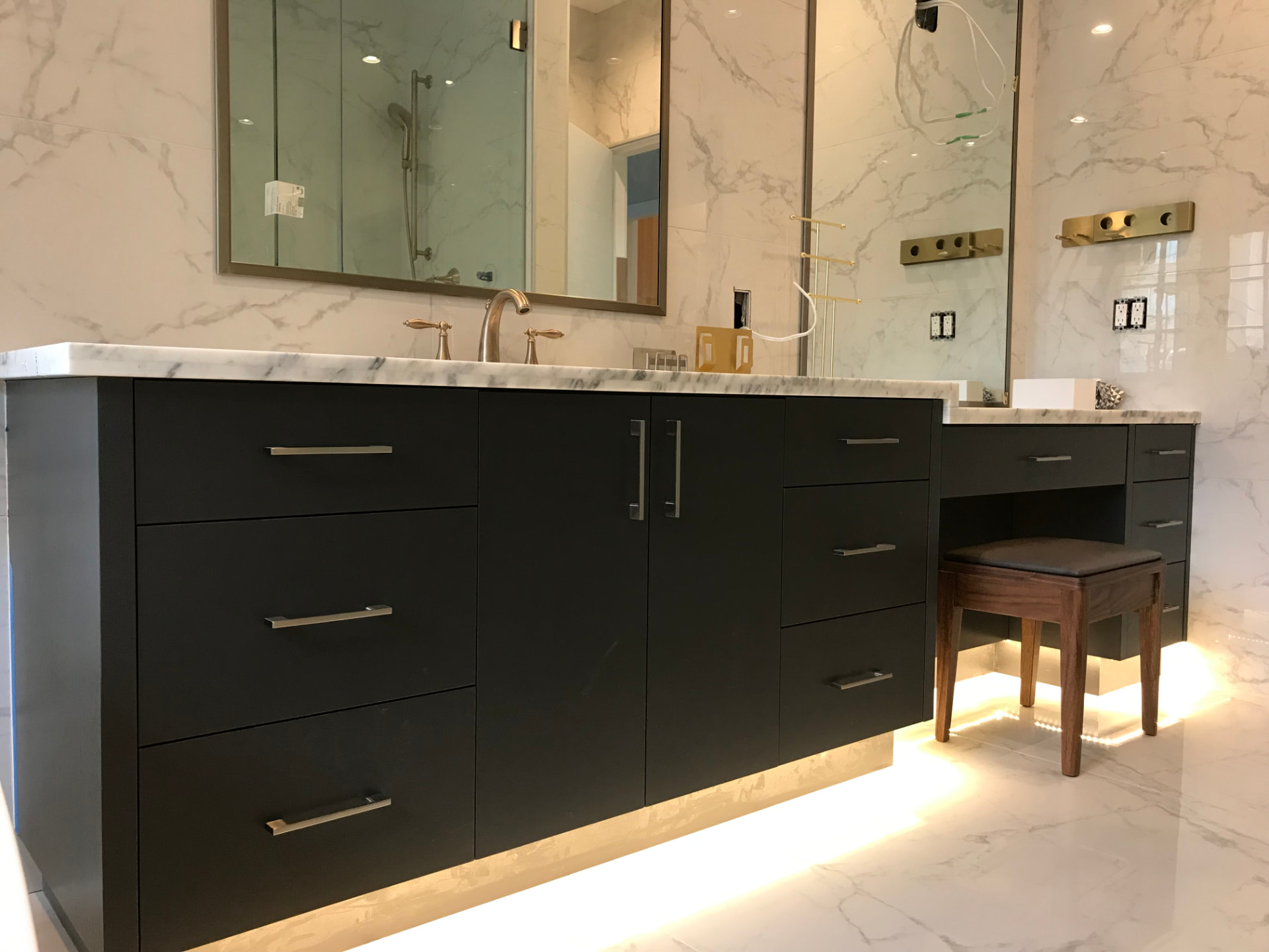 Matte black floating bathroom vanity with white marble counter, walls, and floor, brushed brass faucet, and large mirrors