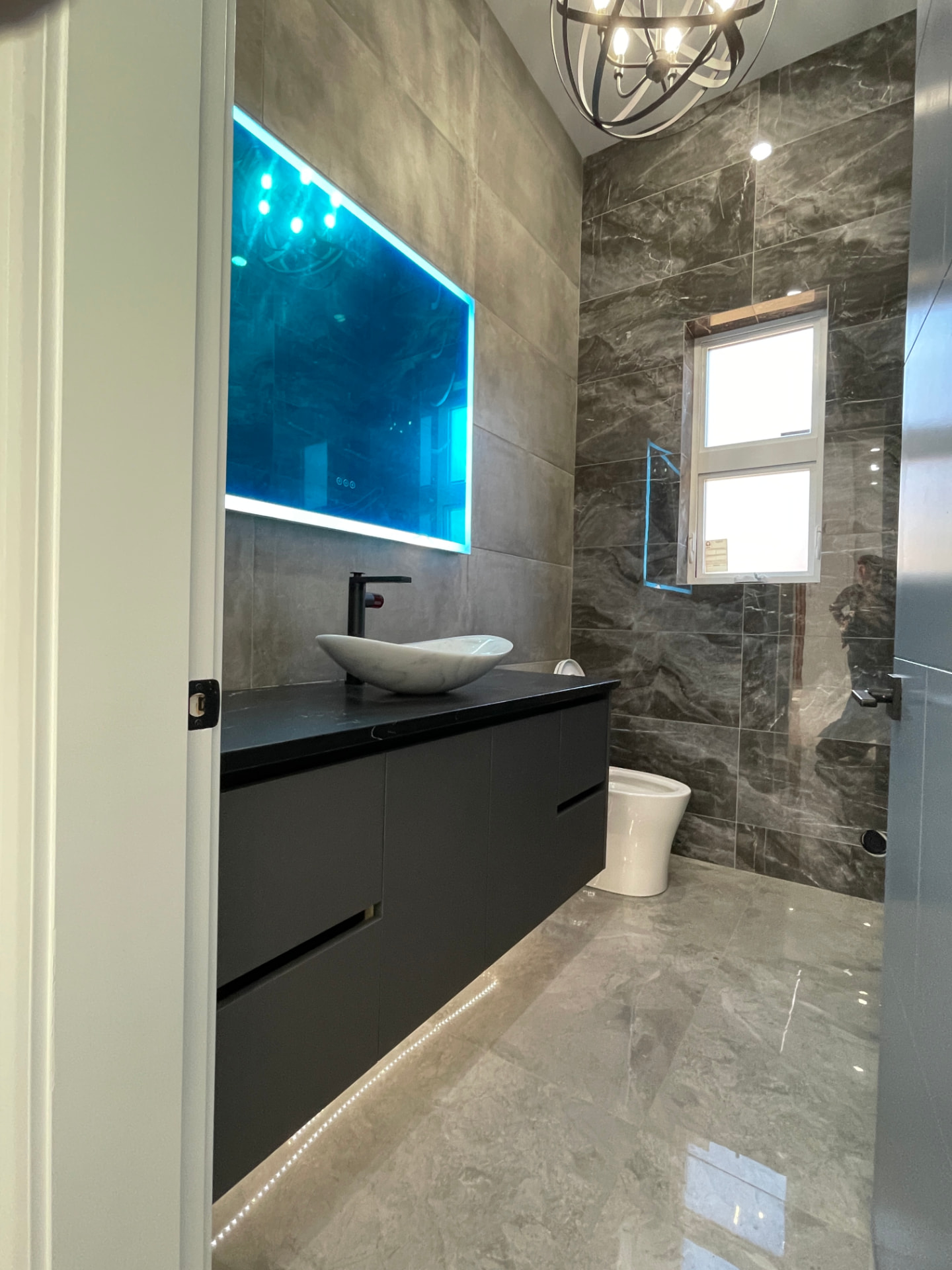 Floating charcoal bathroom vanity with marble vessel sink, matte black faucet, and backlit mirror