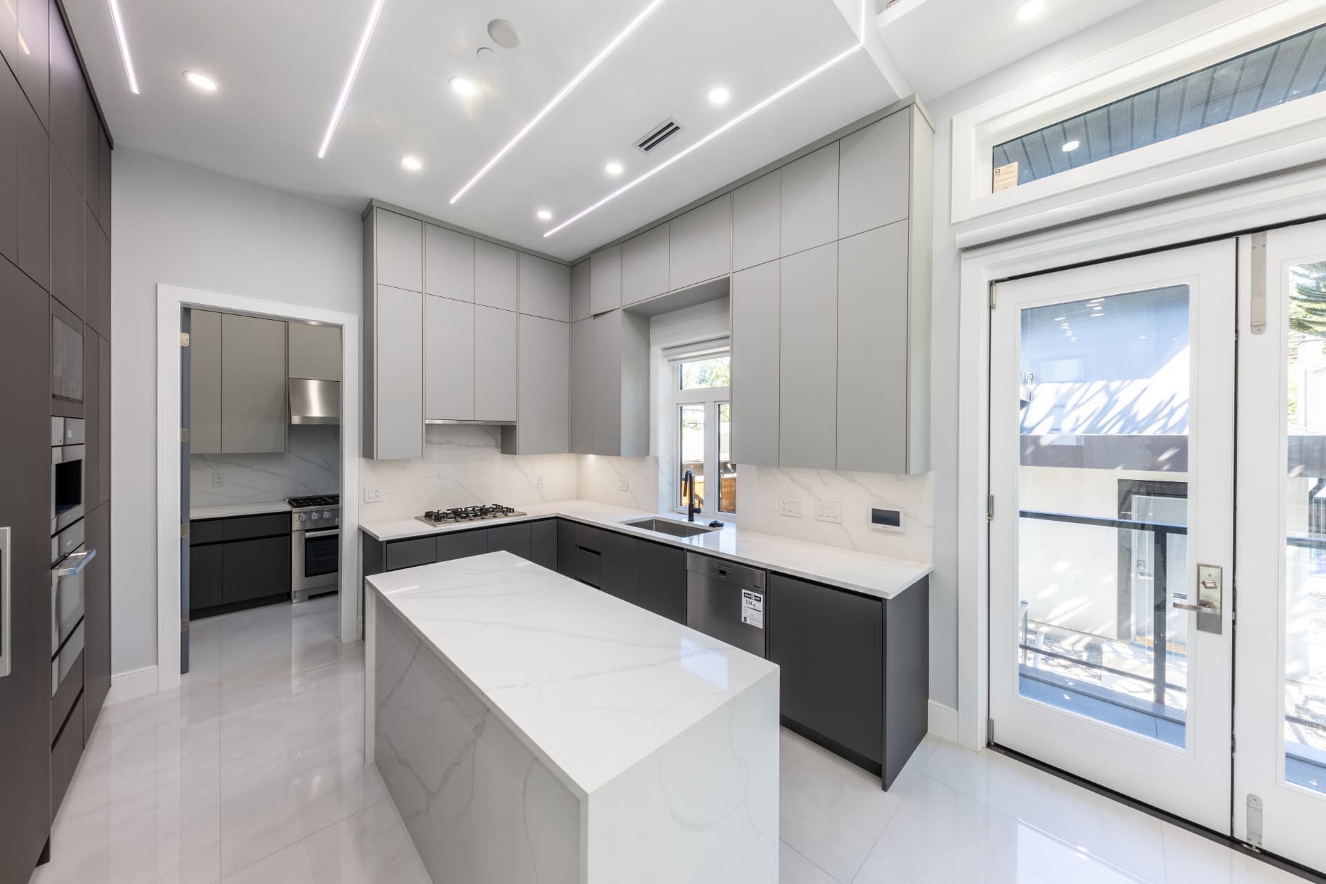 Modern charcoal and white custom kitchen with marble island and glass staircase