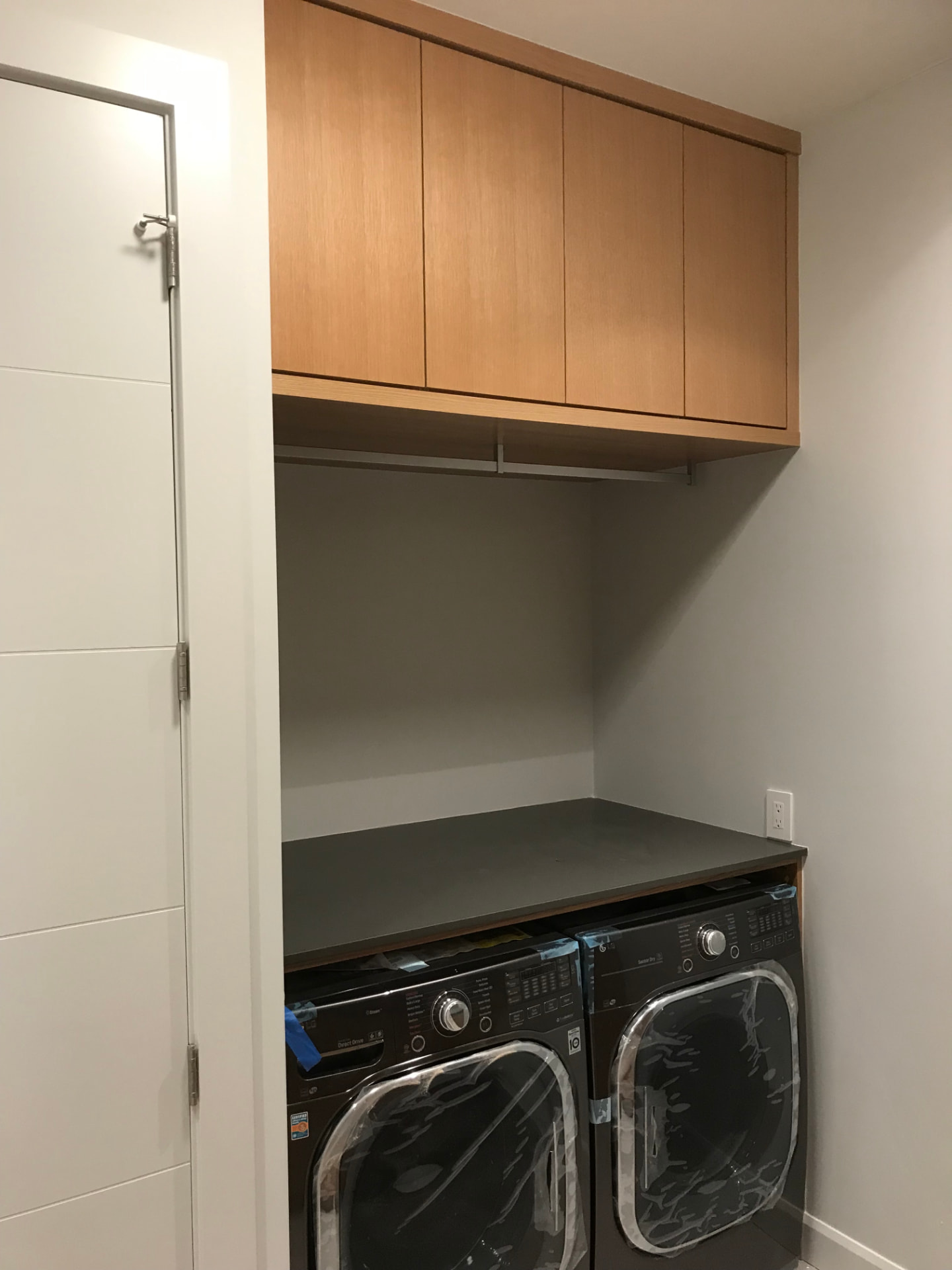 Warm oak laundry cabinetry with black counters over stacked washer and dryer