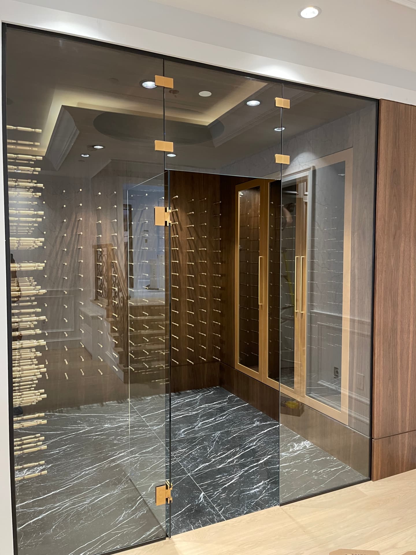 Custom walnut peg wine room with a floor-to-ceiling glass enclosure, brass clamp hinges, wall-mounted bottle pegs, and recessed lighting