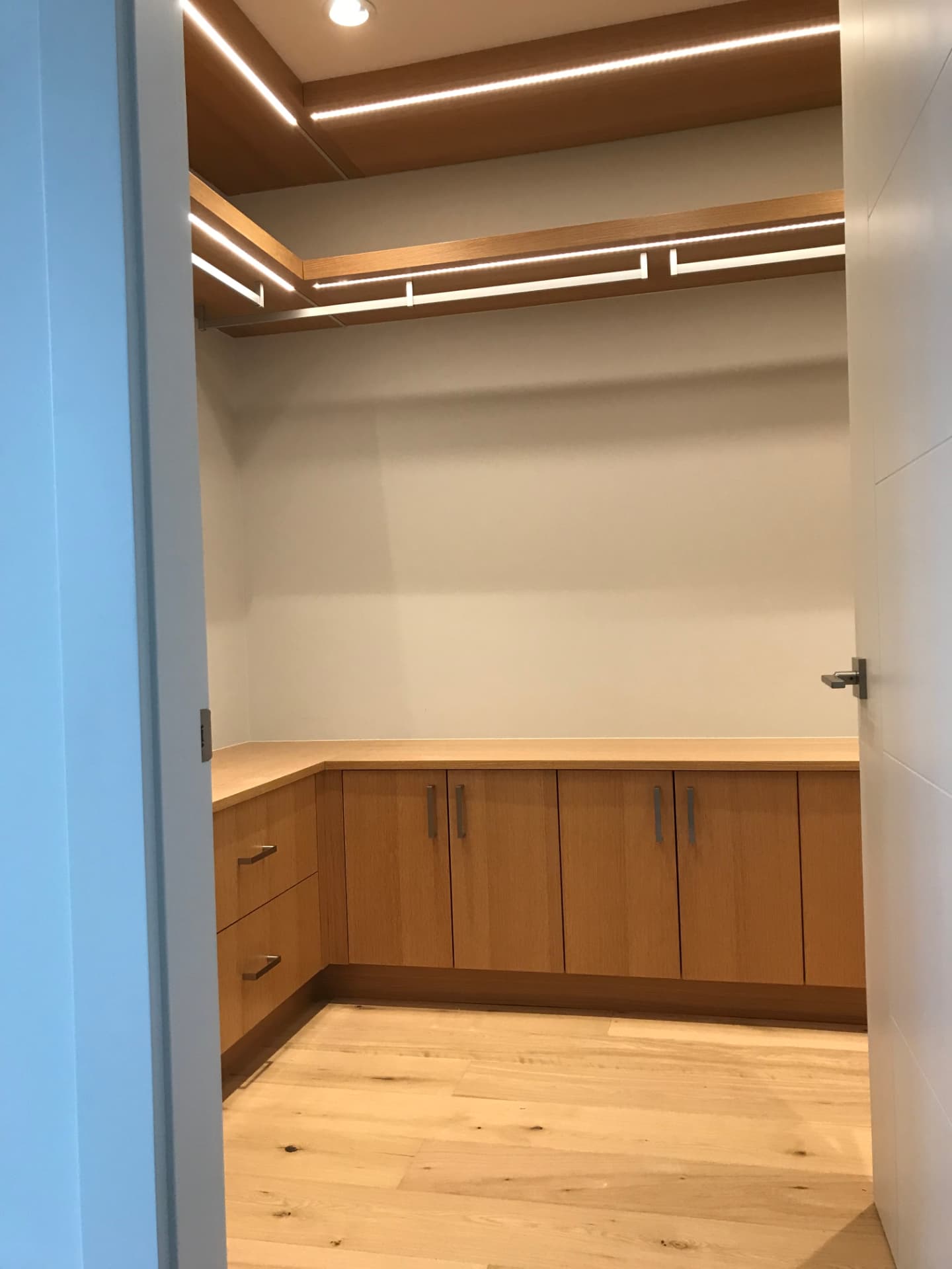 Custom warm wood walk-in closet with illuminated shelving and hanging space