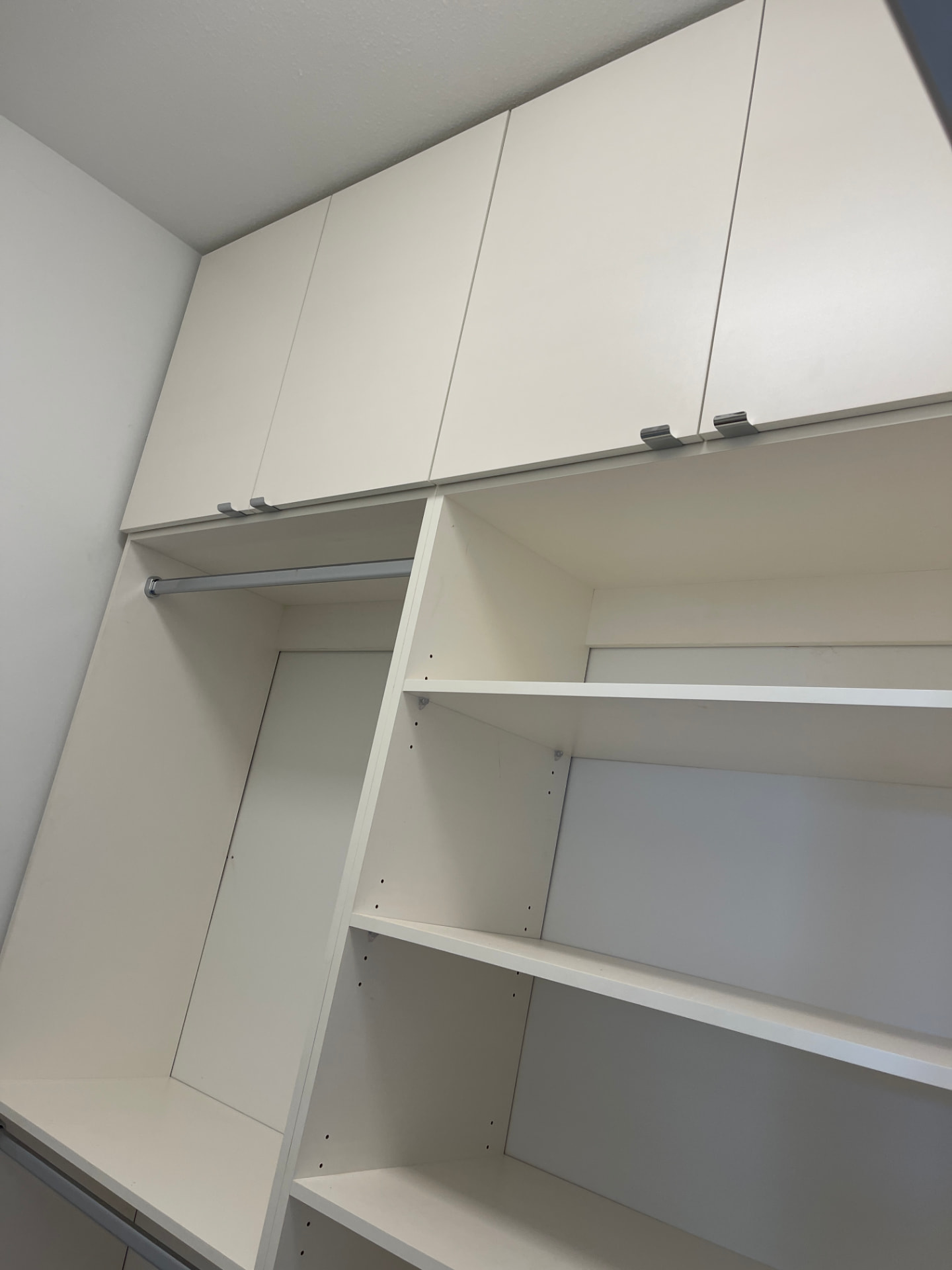 White built-in closet with flat-panel drawer fronts and overhead cabinets, brushed silver edge-pull handles, chrome hanging rods, and adjustable open shelving