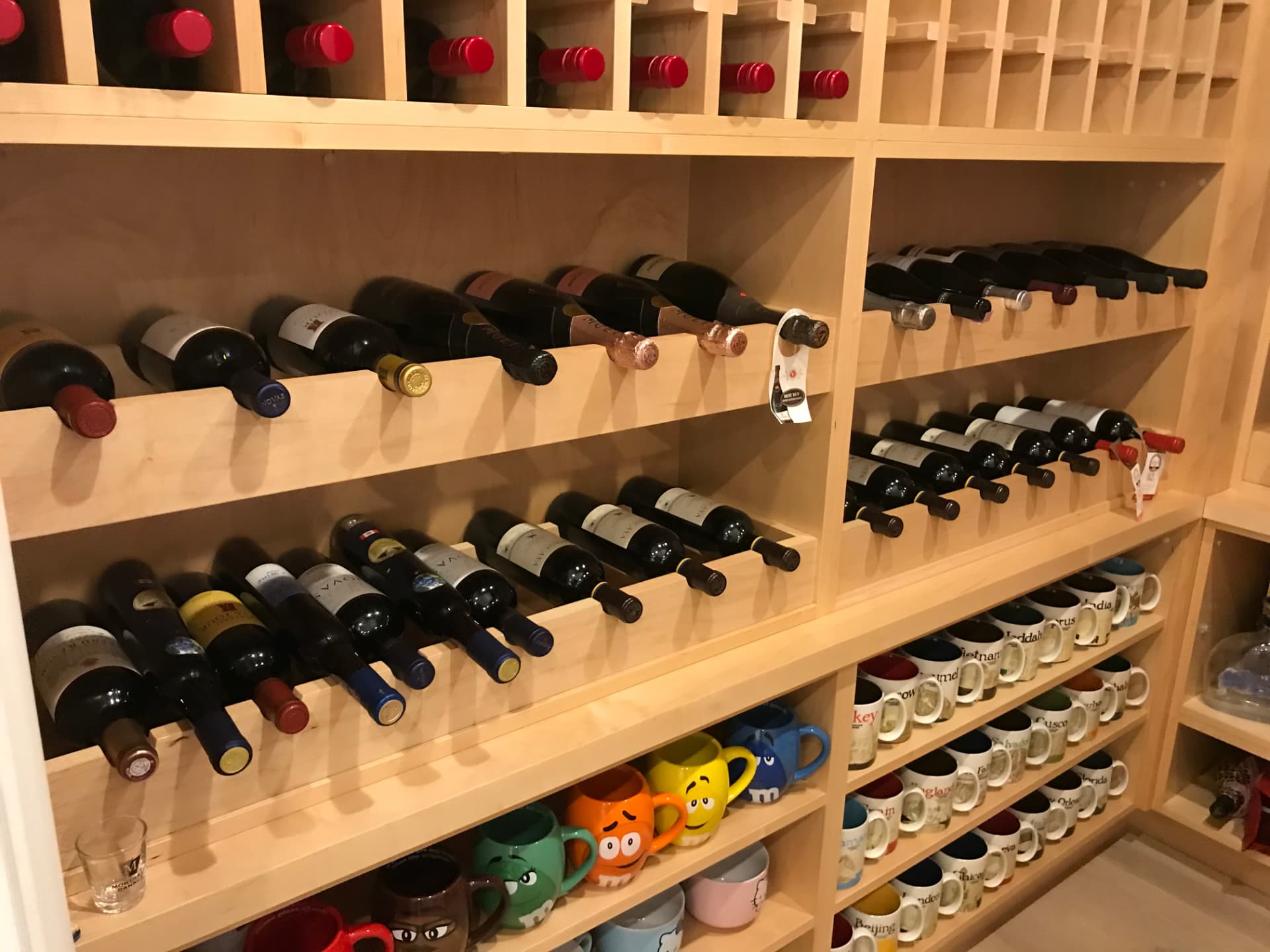 Classic oak walk-in wine room with floor-to-ceiling light-wood cabinetry, individual bottle lattice racks, grid cubbies, cradle shelves, and display shelving, set against deep red walls and ceiling